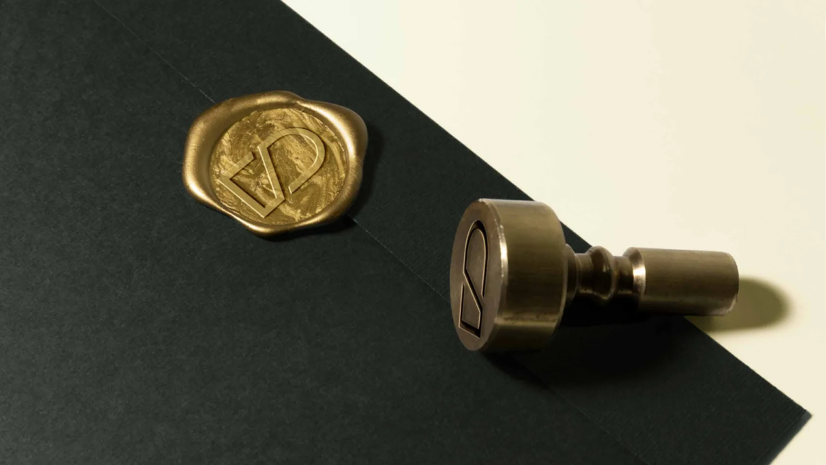 A gold wax seal stamped with the SUB mark on a black envelope, next to a brass seal stamp